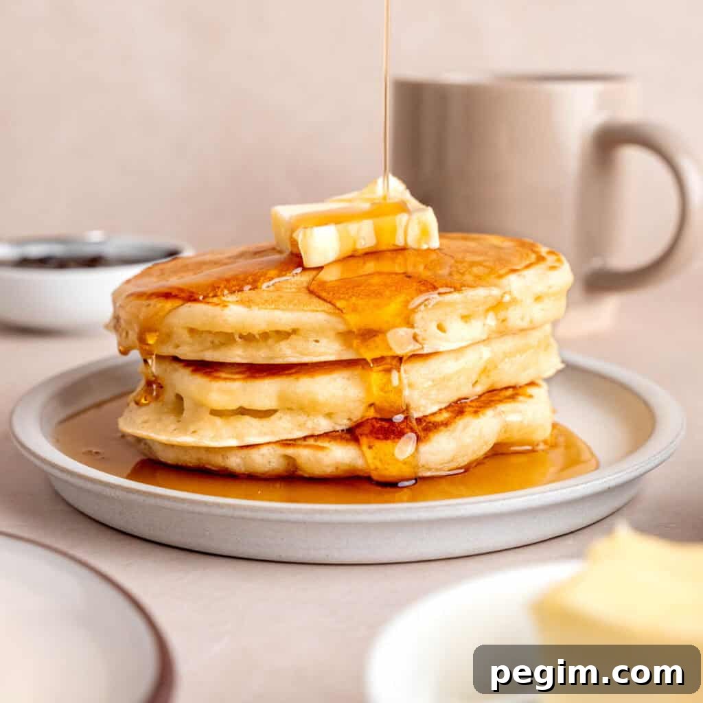Maple syrup getting poured on top of a stack of kefir pancakes.