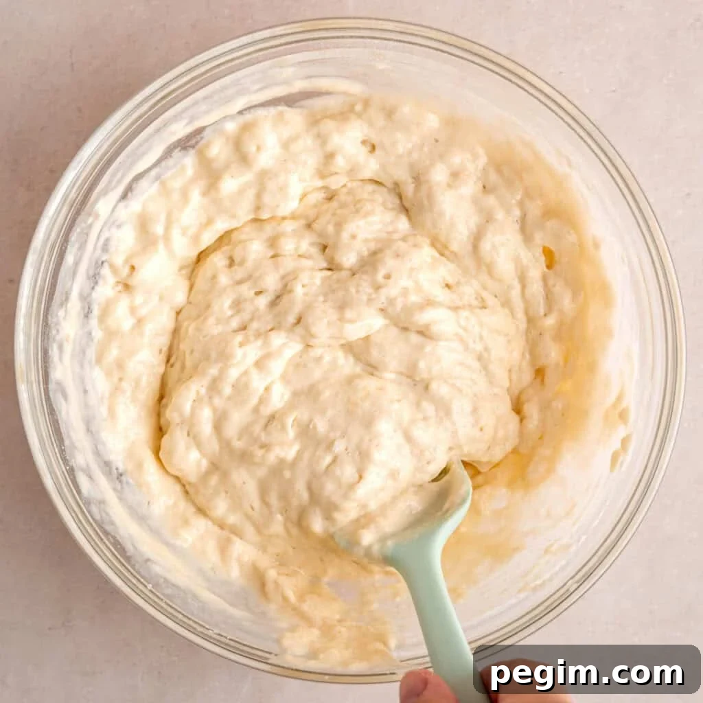 Stirring kefir pancake batter in a bowl with a spatula.