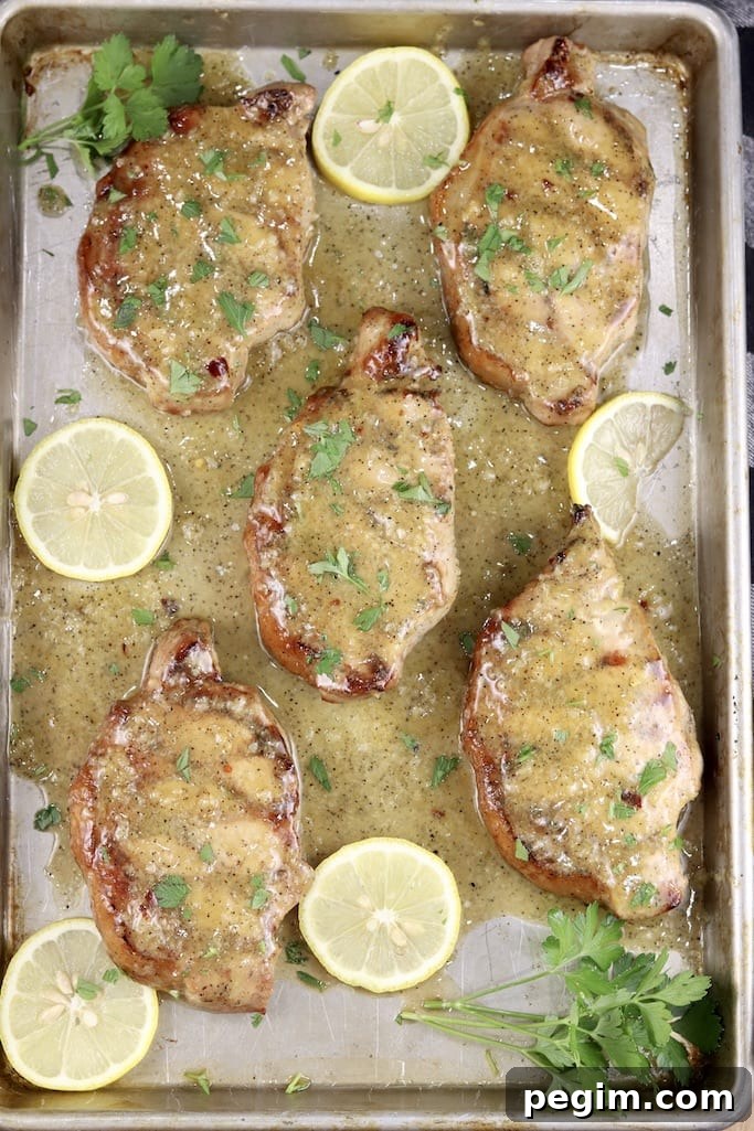 Lemon garlic grilled pork chops, with sliced lemons and parsley on a sheet pan
