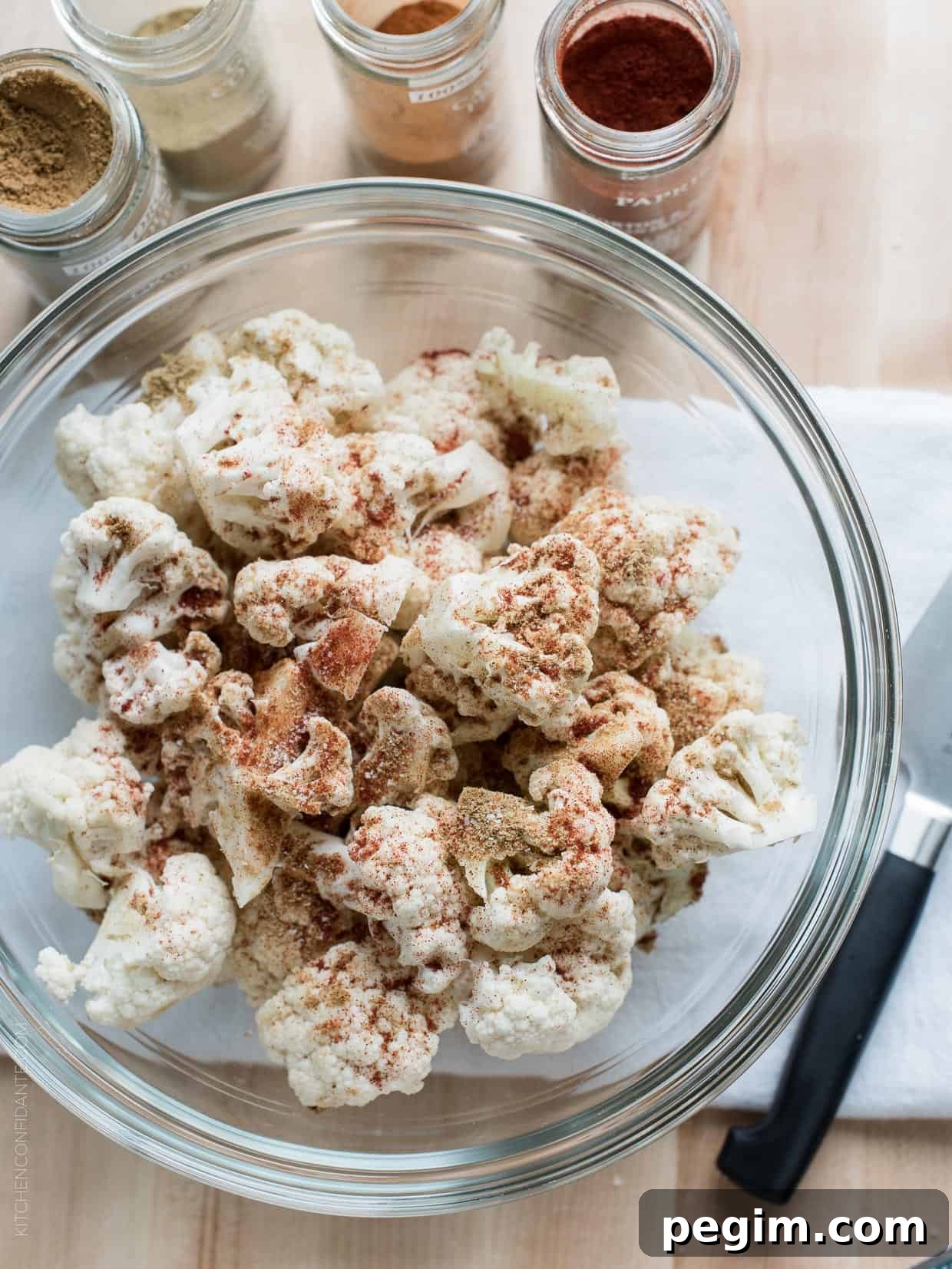 Cauliflower florets sprinkled with spices in a glass bowl.