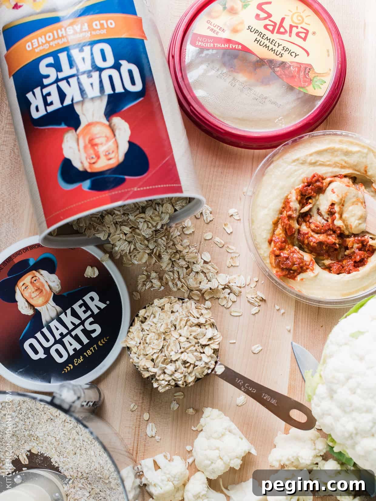 A scoop of old-fashioned oats and a container of hummus on a wooden counter top.