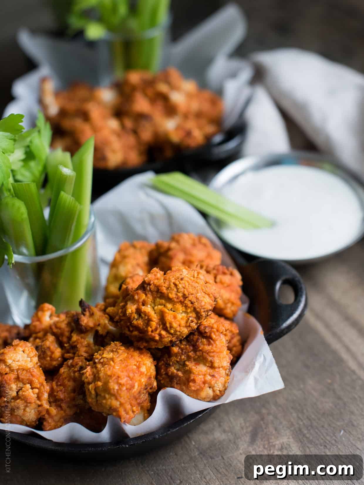 Hummus Battered Buffalo Cauliflower "Wings" served in small cast iron skillets alongside stalks of celery.