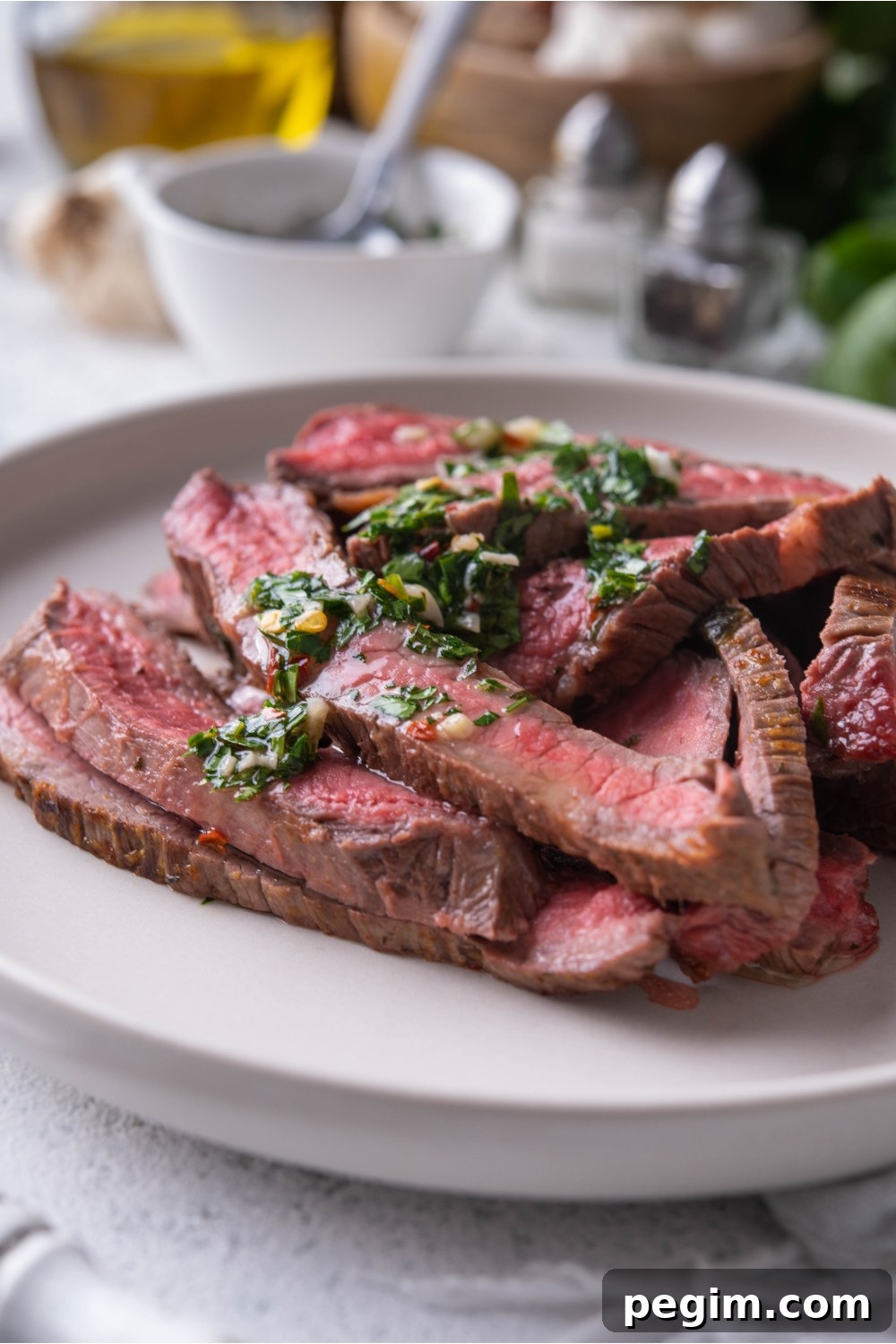 Close up of thinly sliced bavette steak piled on a white plate and covered in chimichurri sauce.