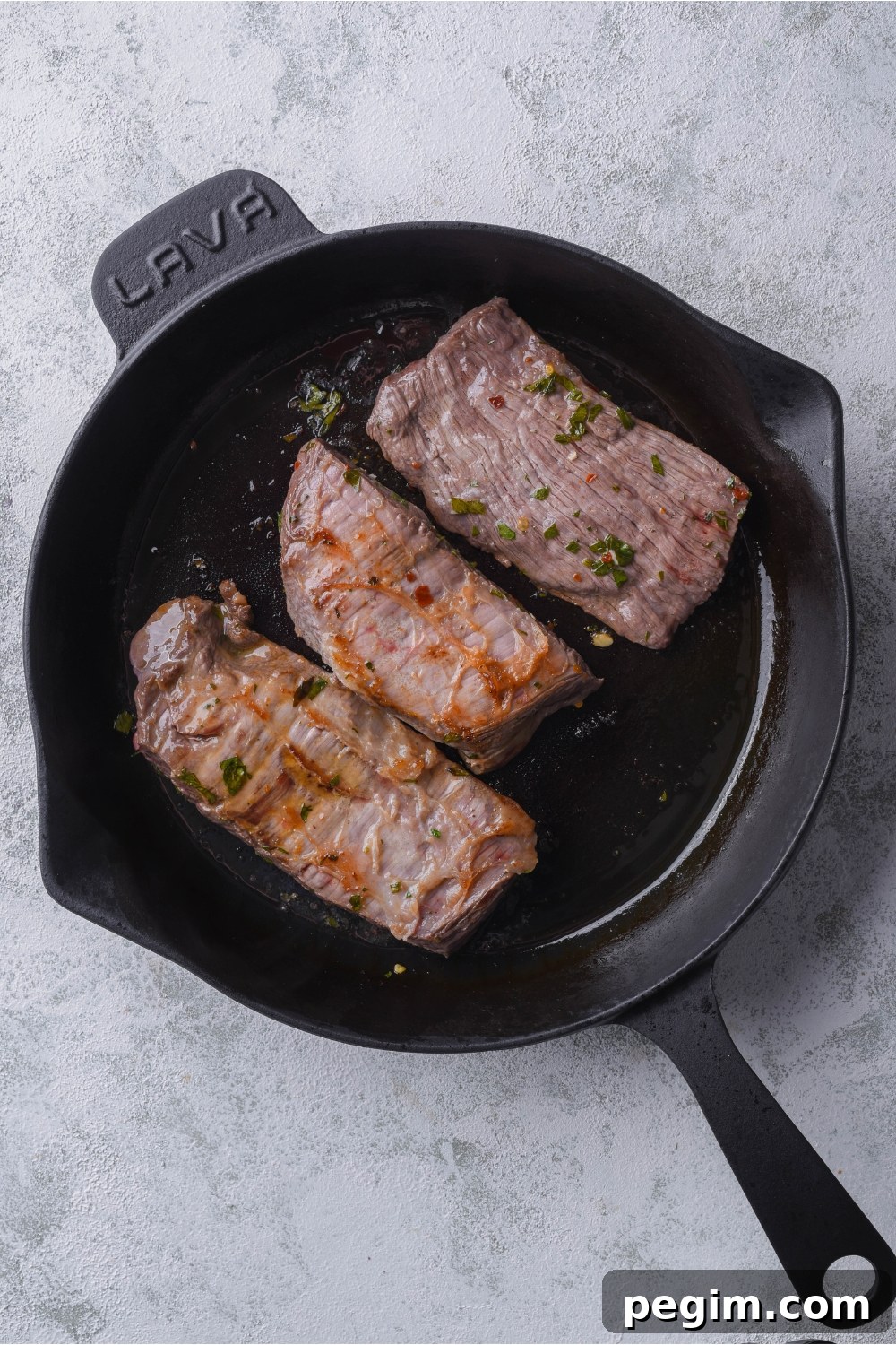 Three seasoned steaks cooking in a black cast iron skillet.