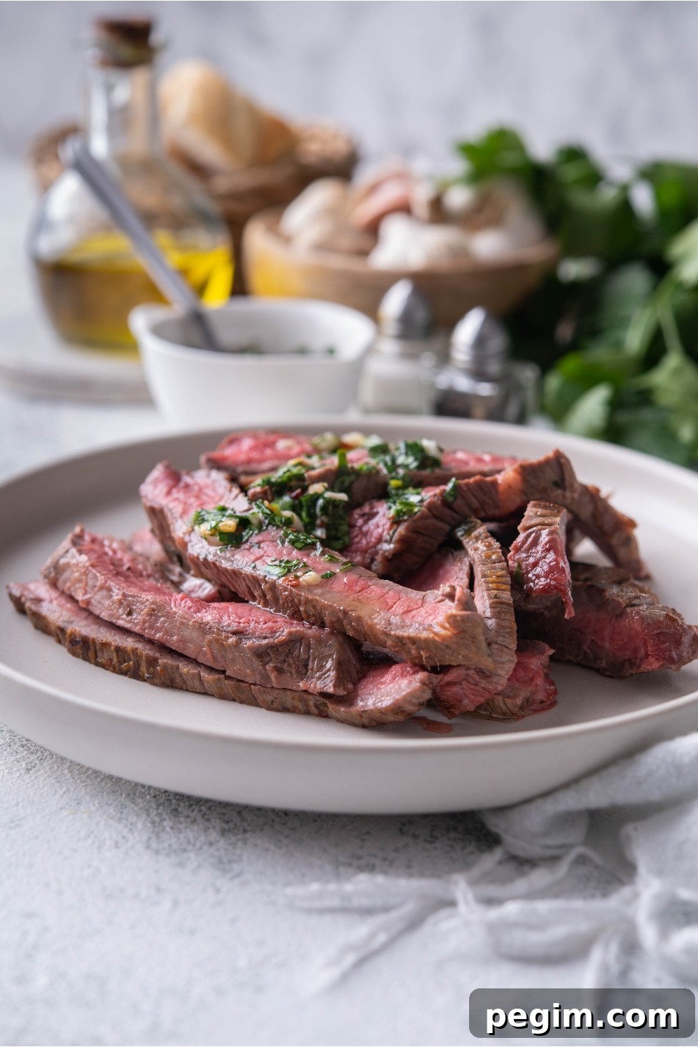 Thinly sliced bavette steak piled on a white plate and covered in chimichurri sauce.