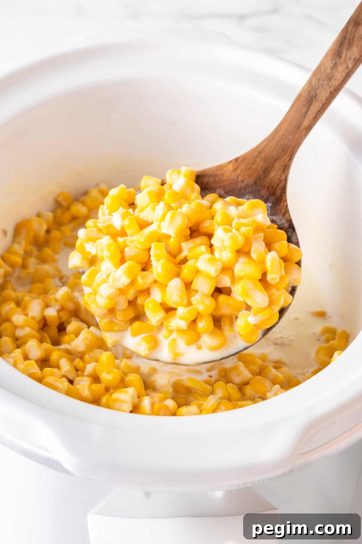 wooden spoon taking creamed corn from the slow cooker