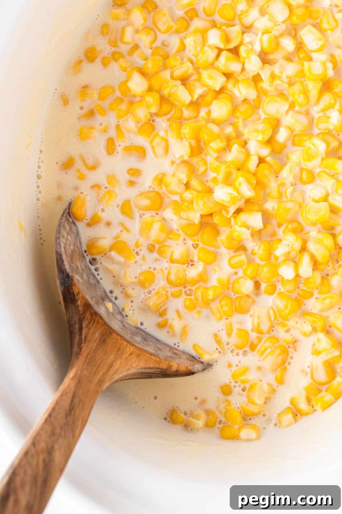 wooden spoon taking creamed corn from the slow cooker