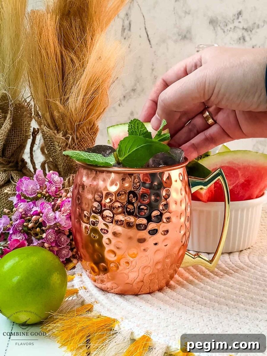 Hand placing watermelon slice into copper mug as a garnish.