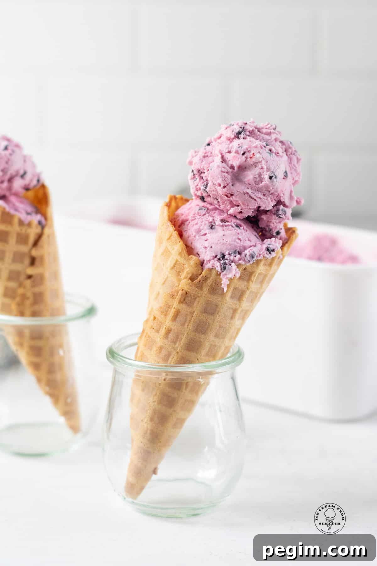 Two small jars holding up waffle cones filled with purple huckleberry ice cream.