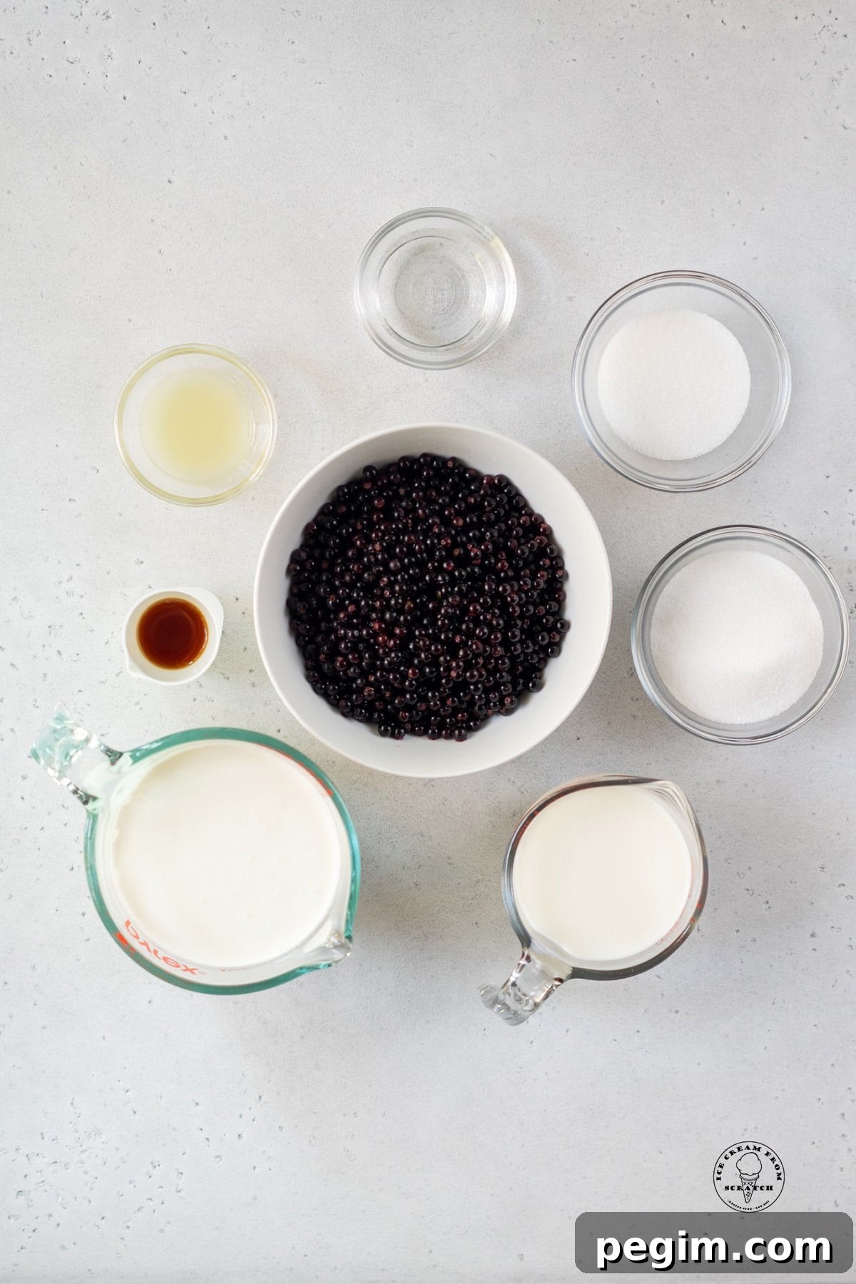 a white bowl filled with huckleberries, surrounded by the other ingredients needed to make huckleberry ice cream.
