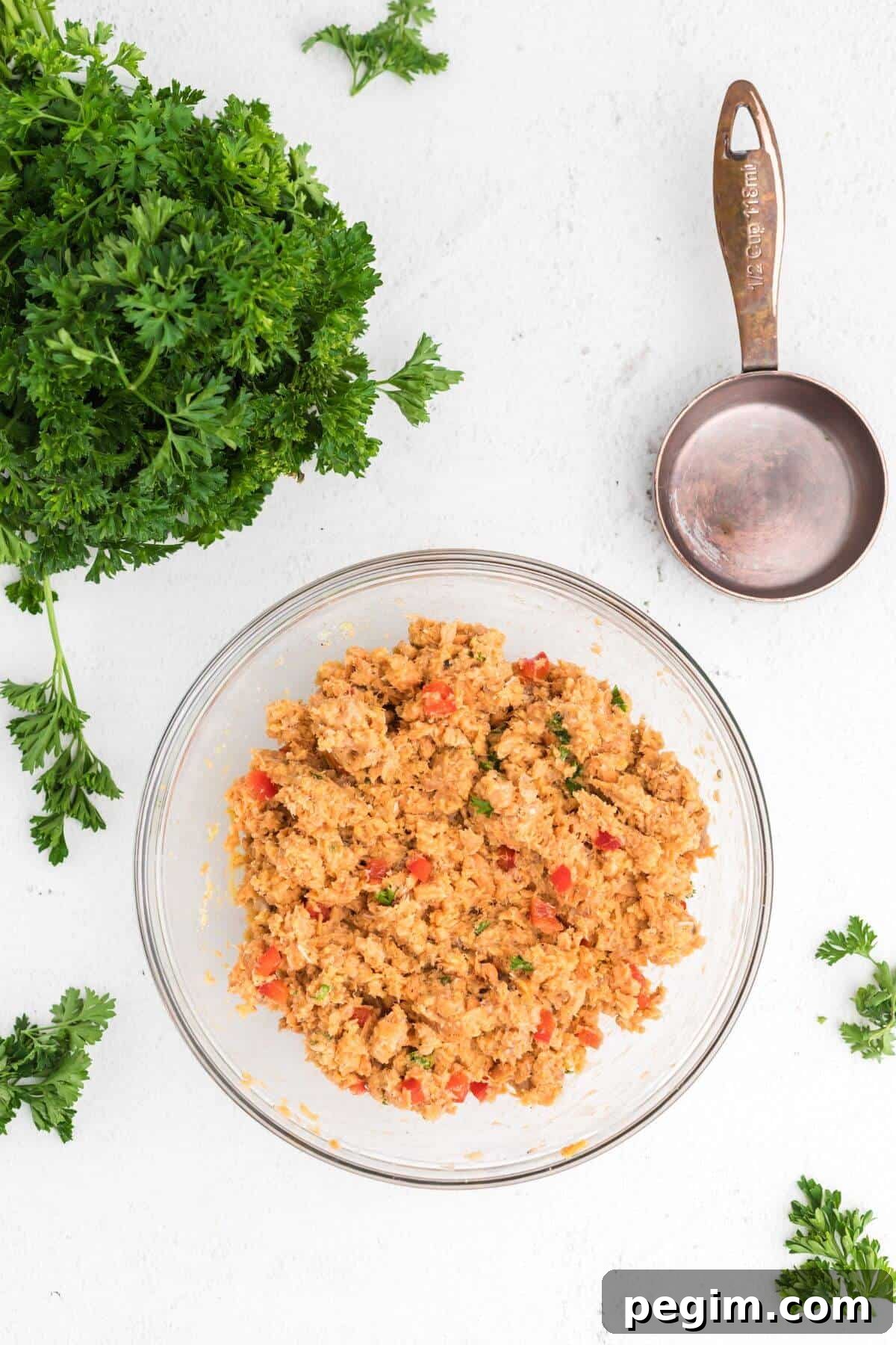 Shredded salmon with chopped bell peppers and seasonings mixed in a clear glass bowl.