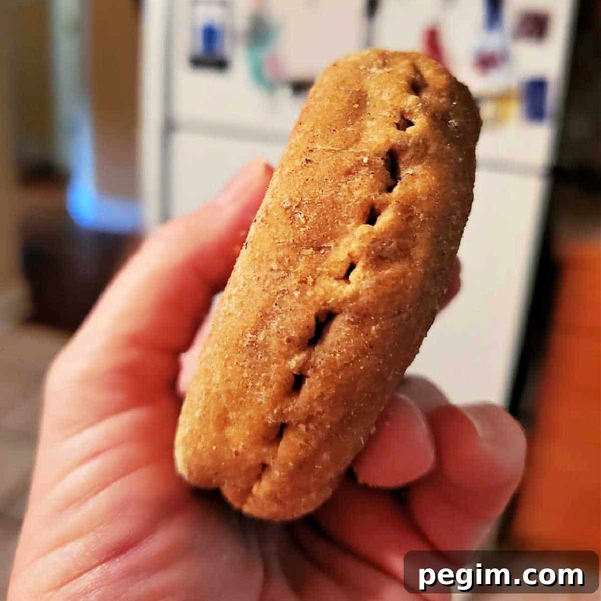 A hand holding an English muffin so you can see the side. It is pierced all along the center line with fork tine marks.