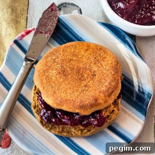 An overhead shot of a split English muffin with jam on it on a striped blue plate.