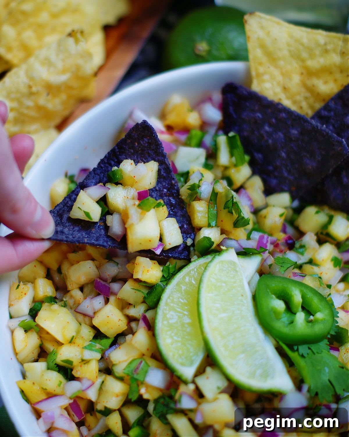 Blue corn tortilla chips and yellow pineapple salsa with lime wedges and jalapeños.