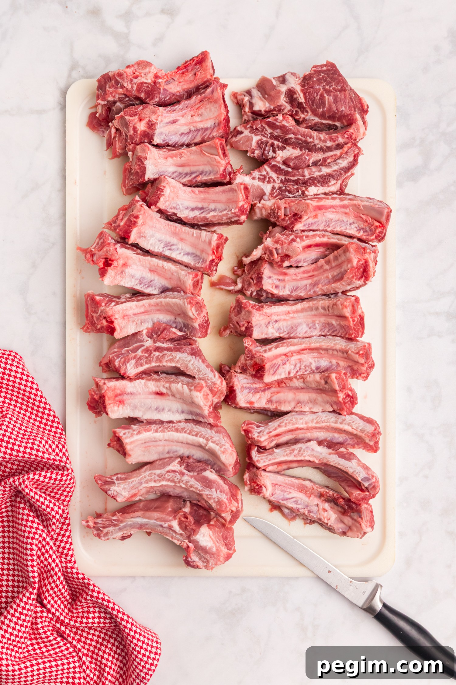 Raw pork ribs cut into individual portions arranged on a white cutting board with a knife beside them.