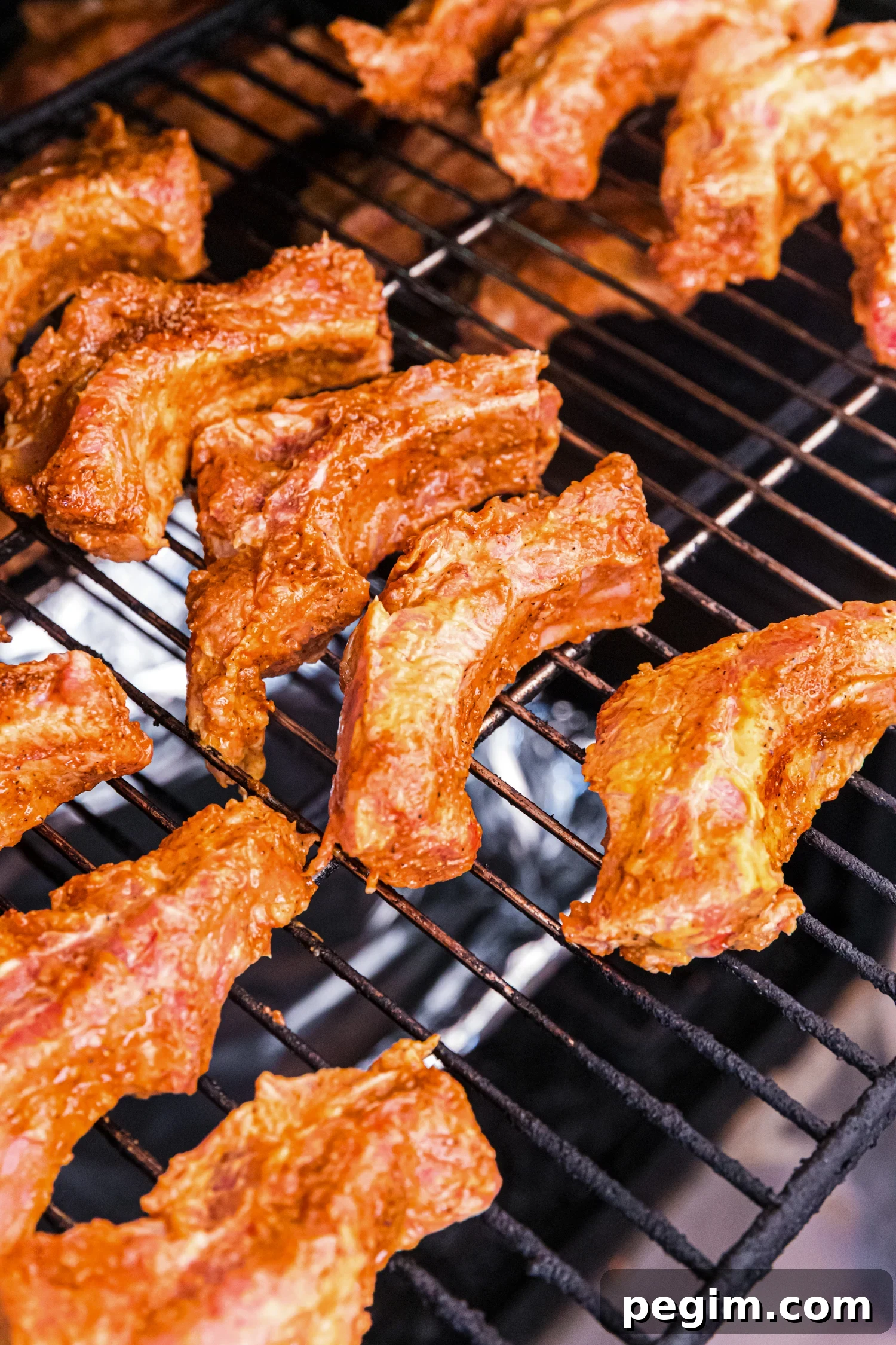 Seasoned pork ribs cooking on a grill grate, lightly browned and spaced apart over indirect heat.