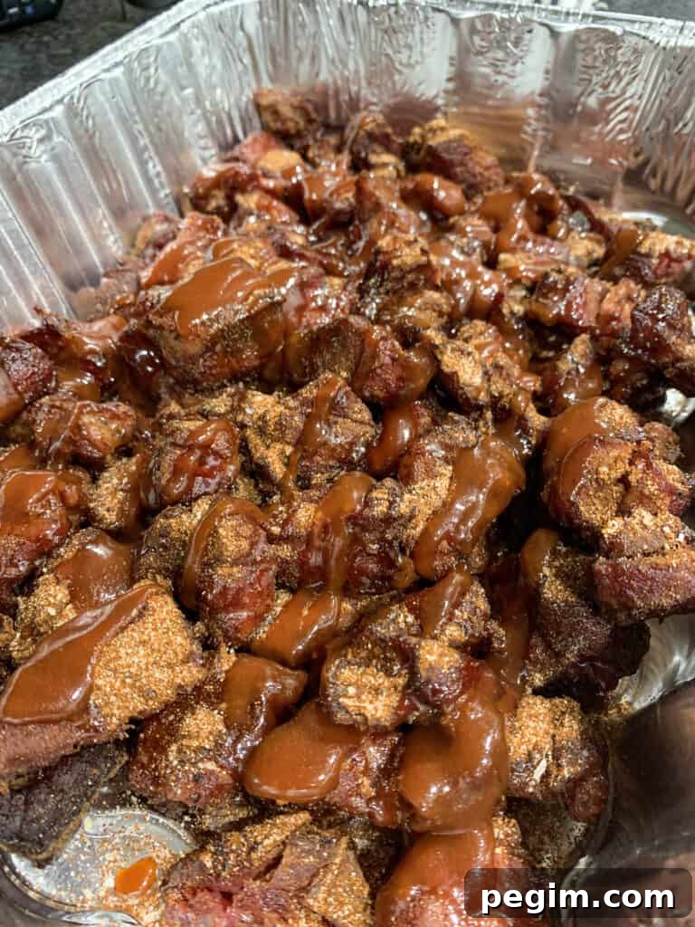pork shoulder chunks in an aluminum pan with rub, barbecue sauce, and honey
