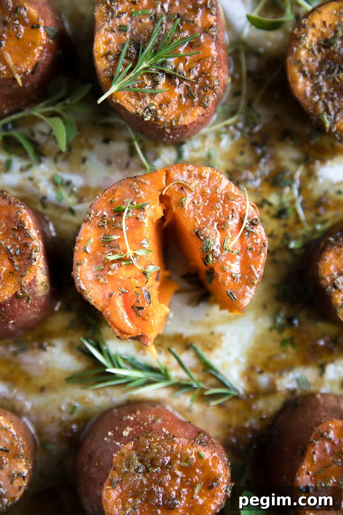Roasted sweet potatoes on a large baking sheet covered with melted butter, brown sugar, and fresh herbs.