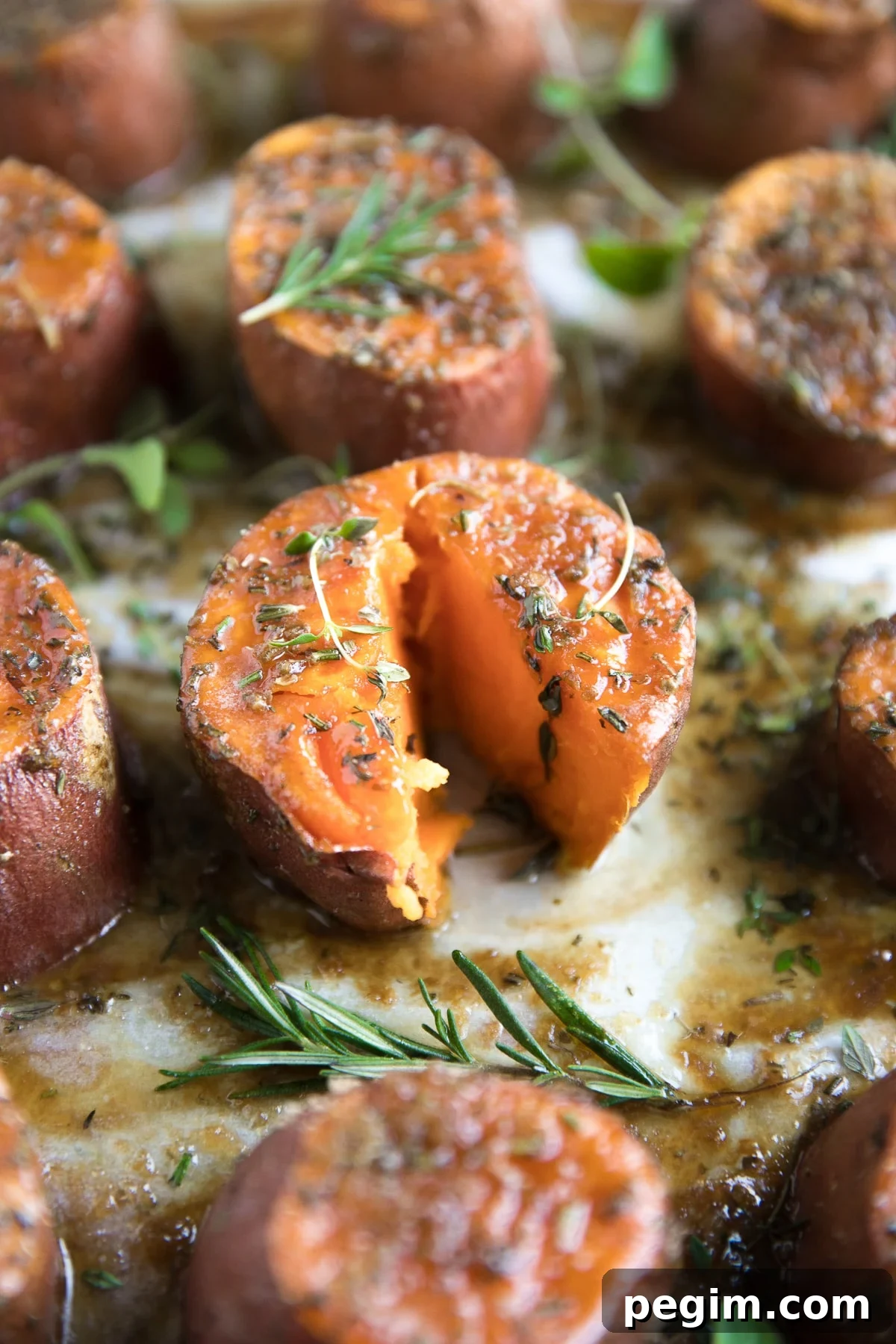 Tender oven-roasted sweet potatoes on a large baking sheet covered with melted butter, brown sugar, and fresh herbs.