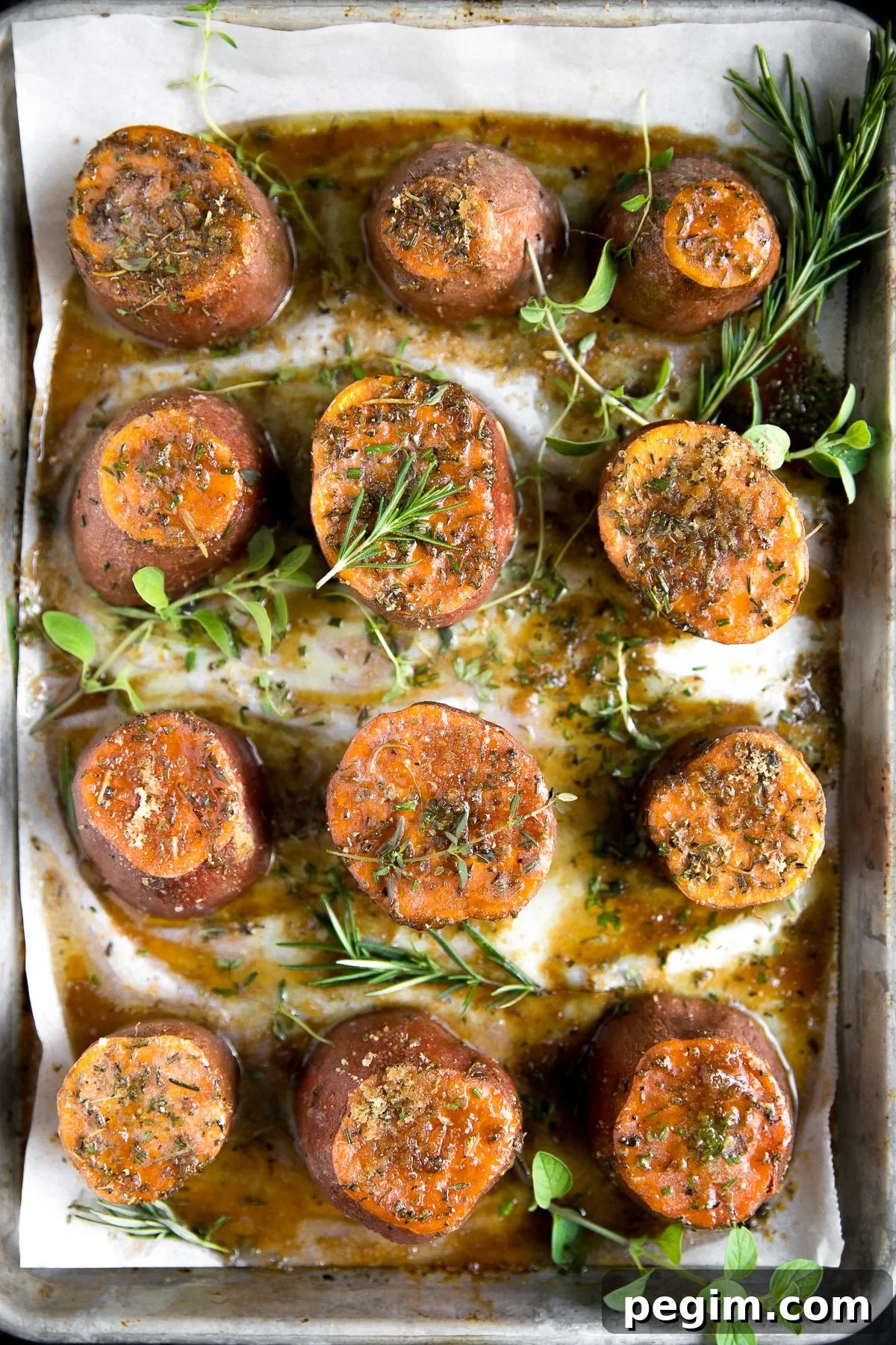 Overhead image of Tender oven-roasted sweet potatoes on a large baking sheet covered with melted butter, brown sugar, and fresh herbs.