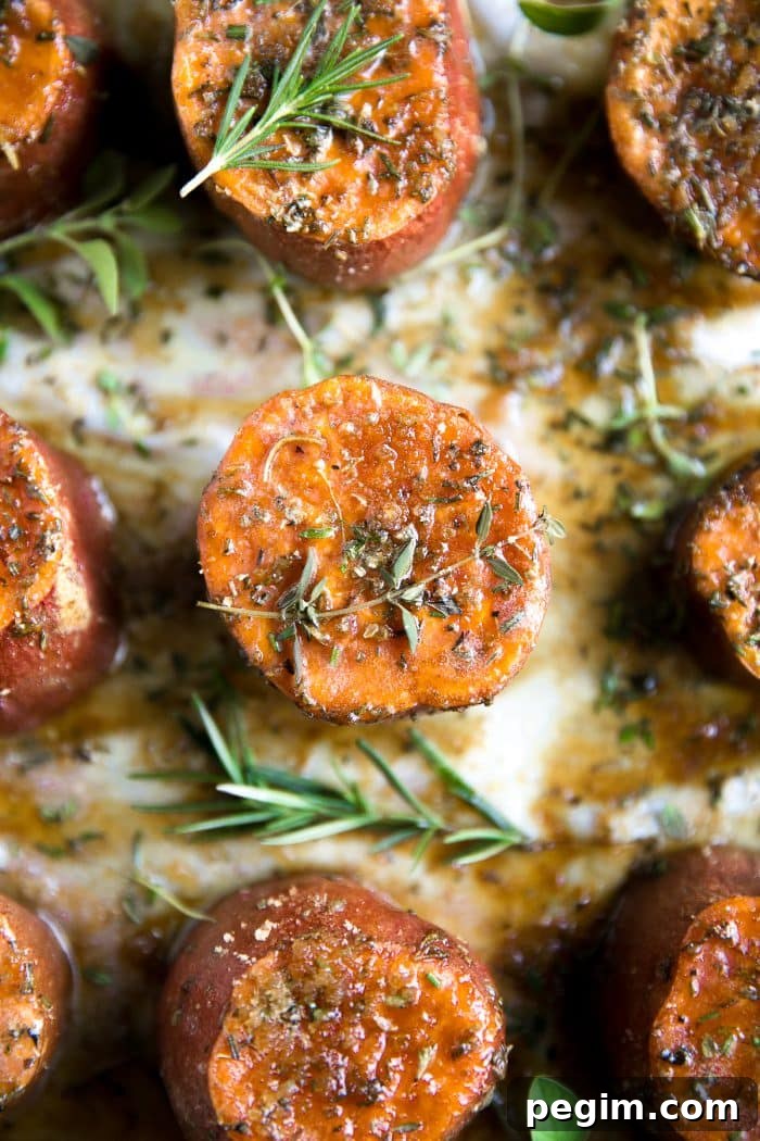 Roasted sweet potatoes on a large baking sheet covered with melted butter, brown sugar, and fresh herbs.