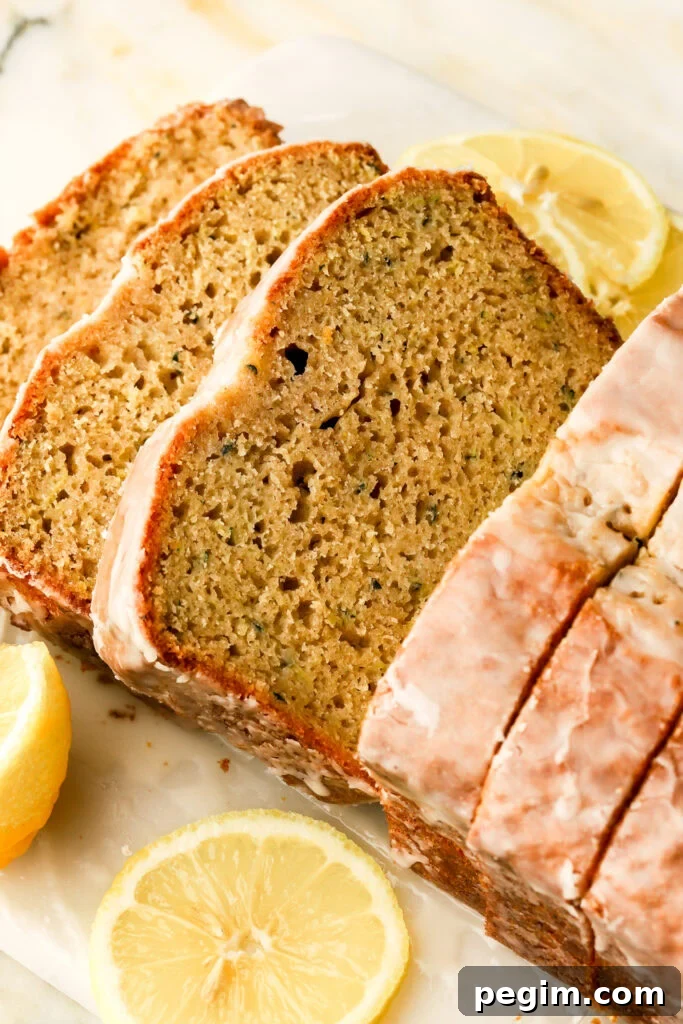 lemon zucchini bread with lemon glaze sliced on a cutting board with lemons