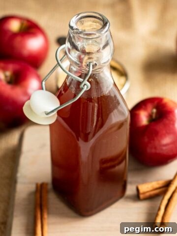 A bottle of apple brown sugar syrup, with apples and cinnamon sticks.