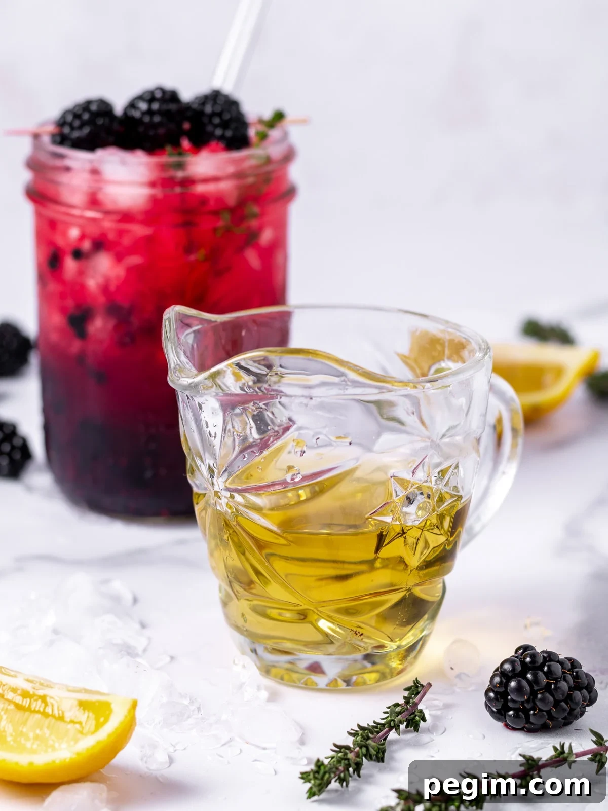 small glass of thyme simple syrup, lemon wedges, thyme sprigs and a blackberry mocktail in a mason jar
