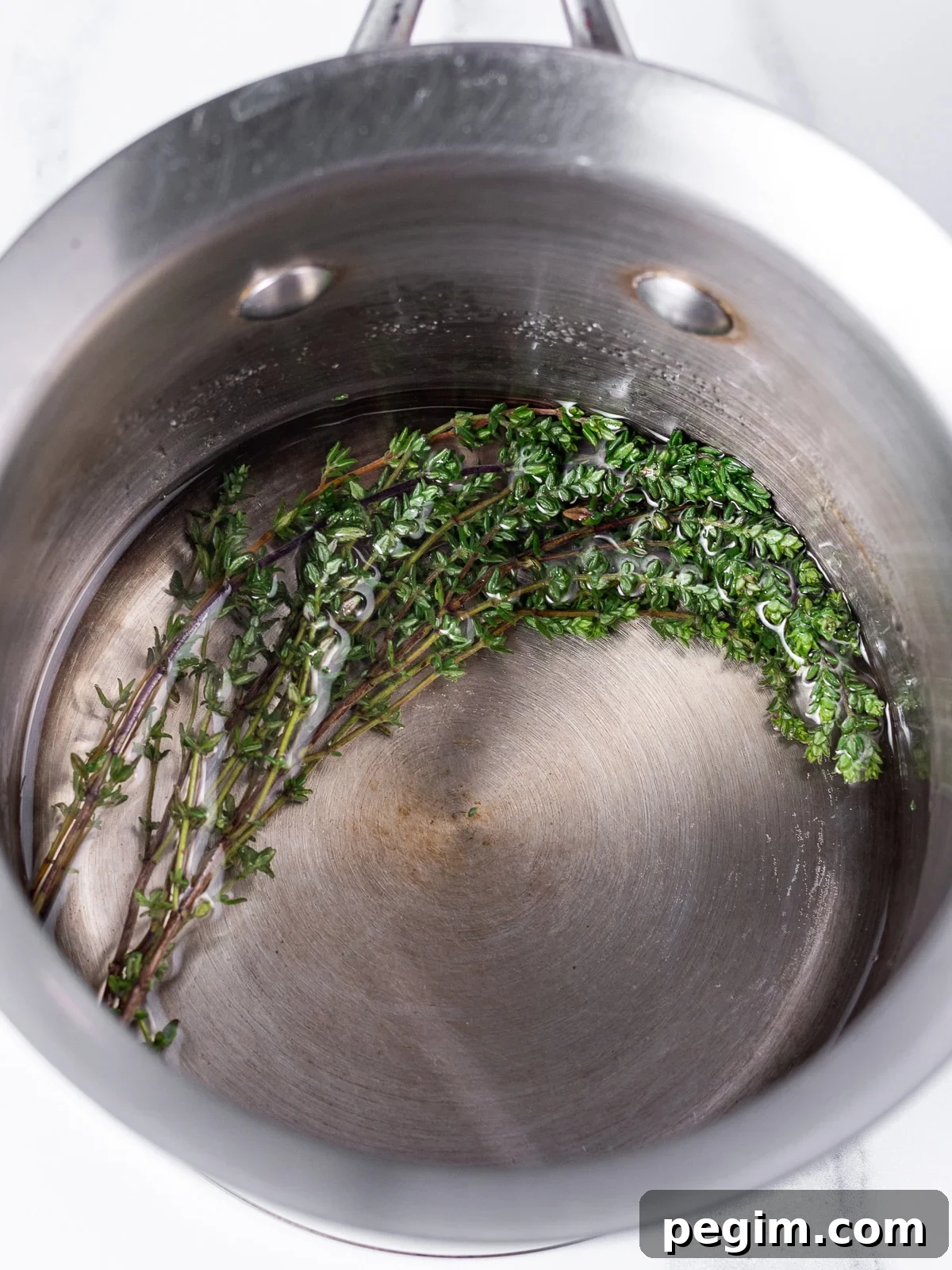 saucepan with sugar dissolving into water and fresh thyme sprigs