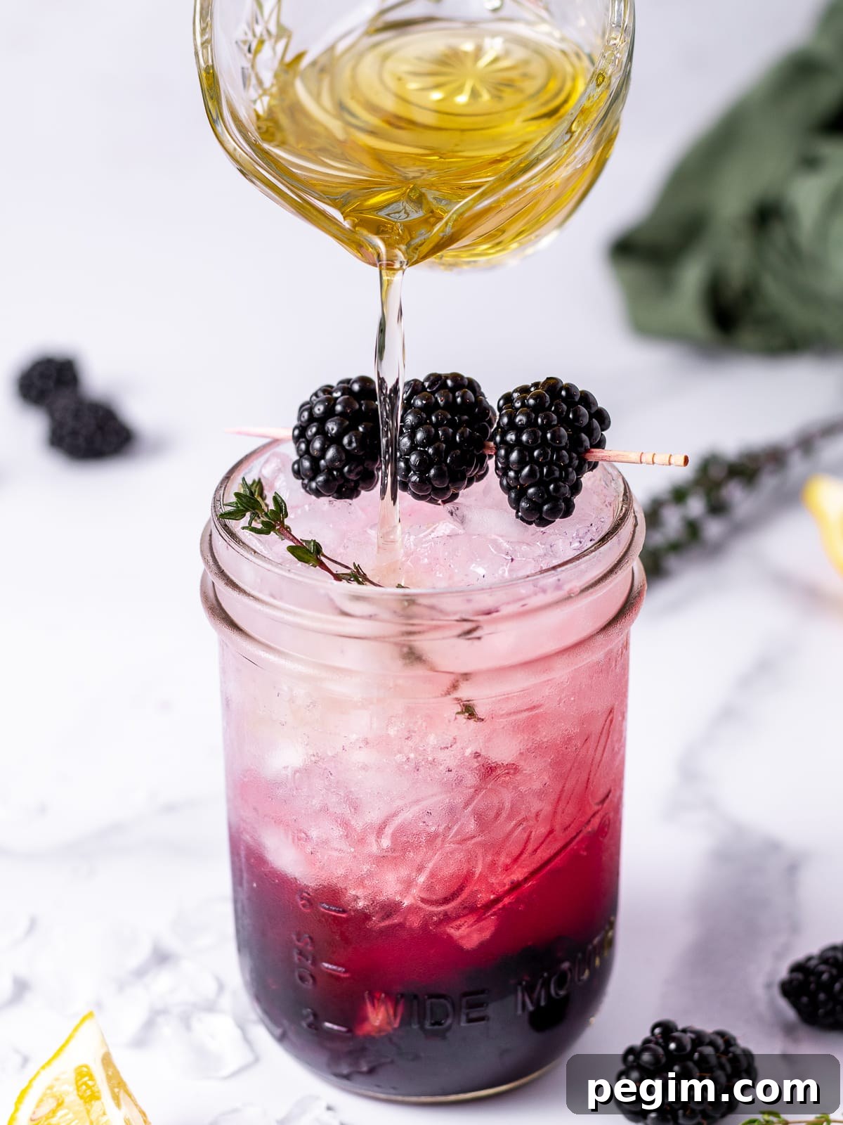 pitcher of thyme simple syrup being poured into a fizzy blackberry mocktail