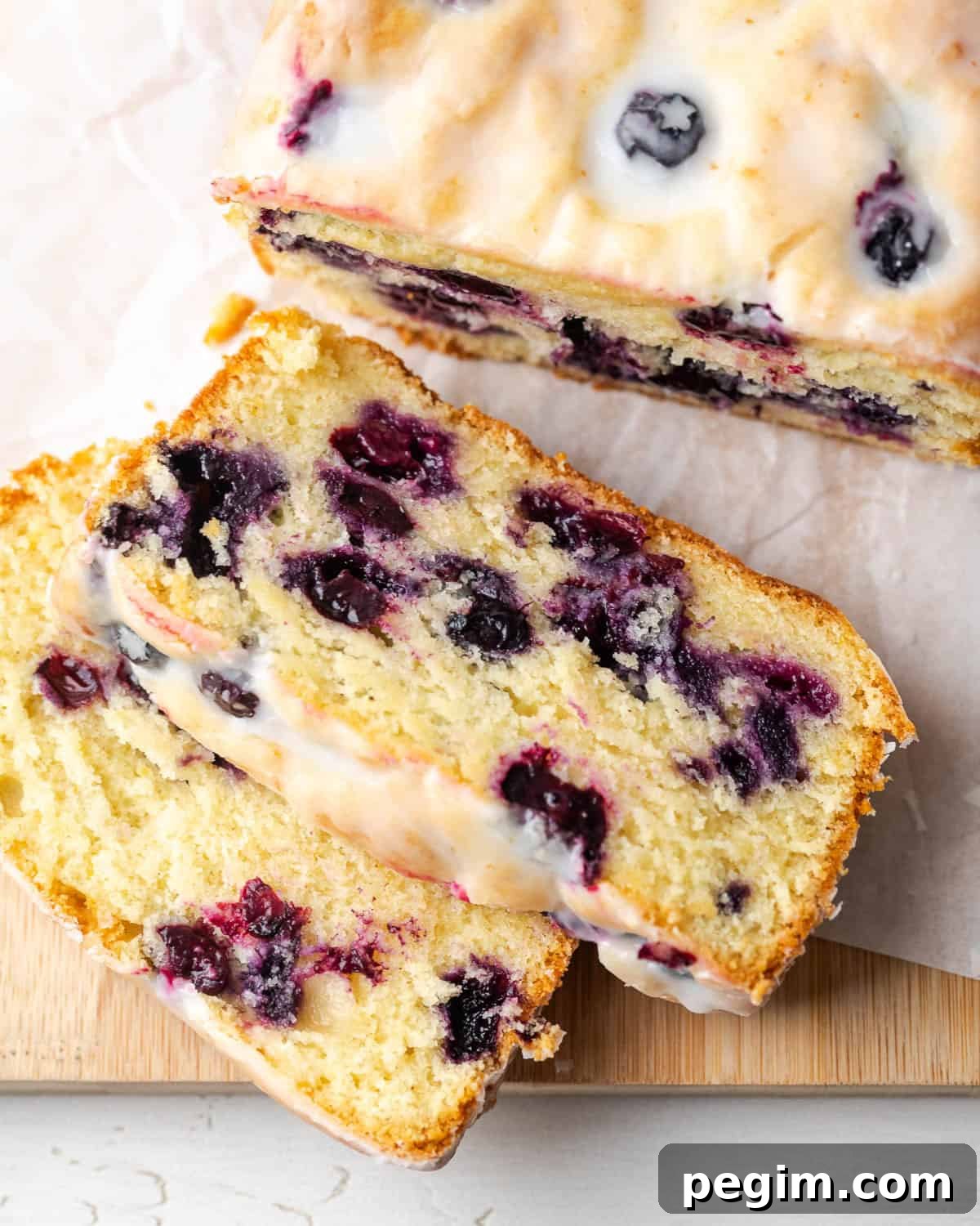 A loaf of lemon blueberry pound cake cut into slices sitting on a wooden cutting board. 
