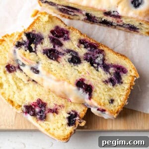 A loaf of lemon blueberry pound cake cut into slices and sitting on a wooden cutting board.