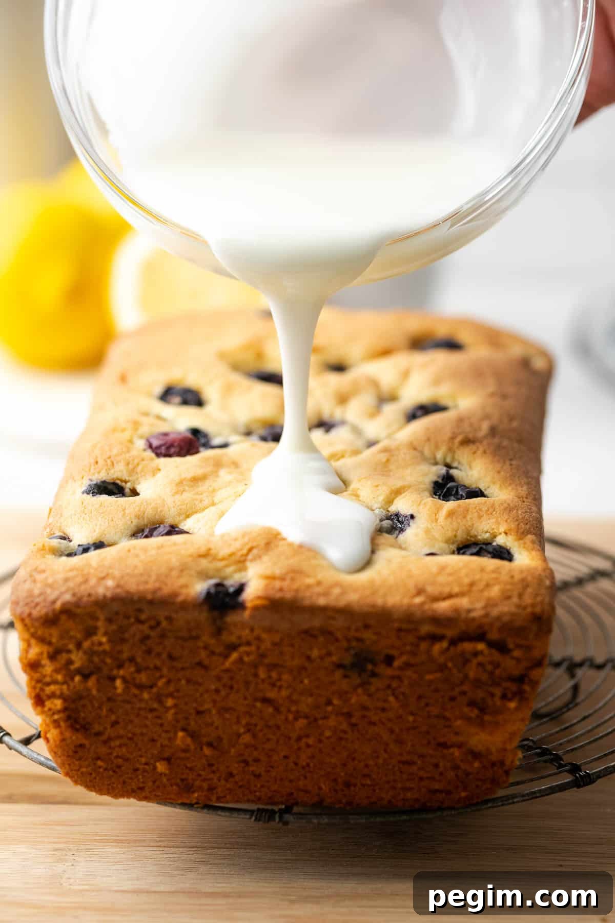 Lemon glaze being poured over a cooled lemon blueberry pound cake. 