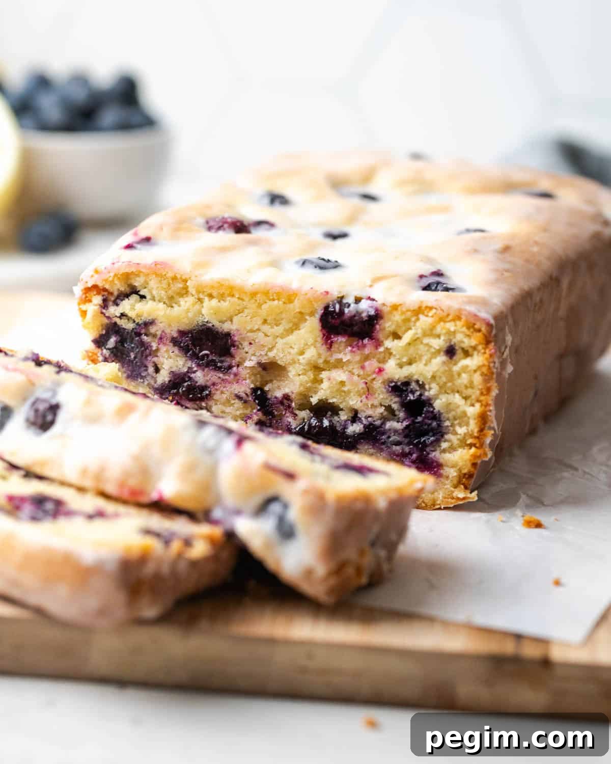 A loaf of lemon blueberry pound cake cut into slices and sitting on a wooden cutting board.