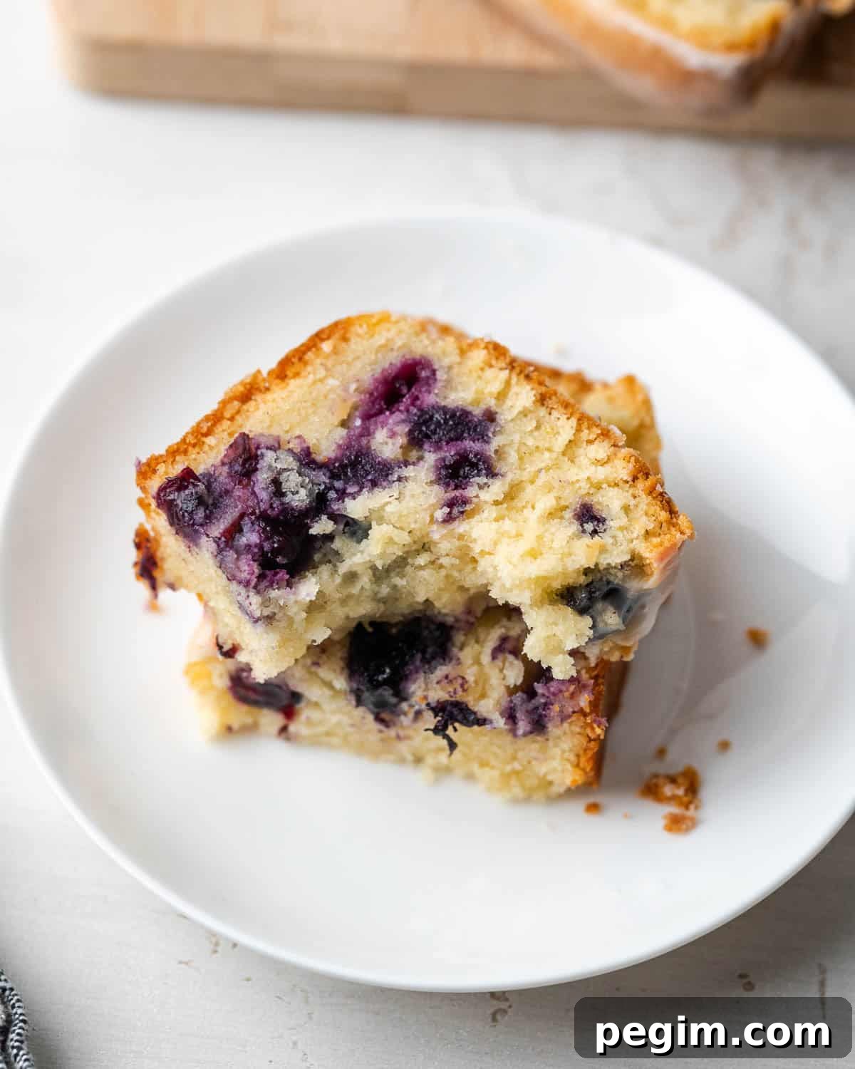 A slice of lemon blueberry pound cake with a bite taken out sitting on a small dessert plate.