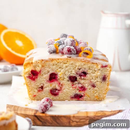A loaf of cranberry orange pound cake sitting on a wooden cutting board.