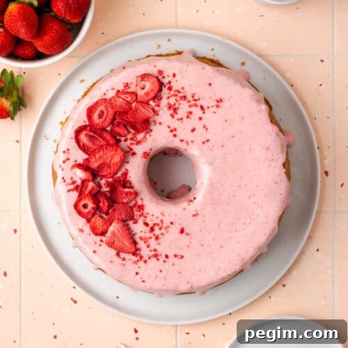A strawberry pound cake on a white serving plate sitting on a pink table.