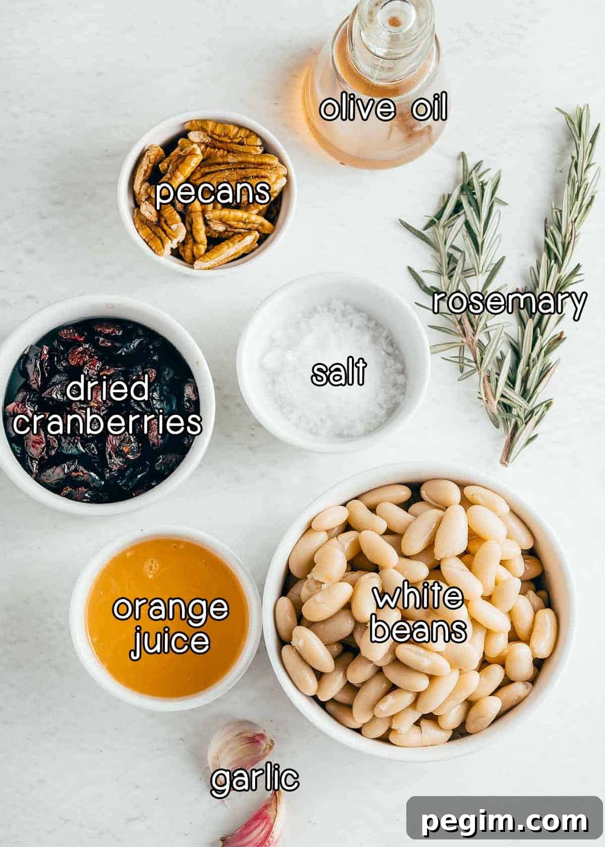 Overhead shot of ingredients - olive oil, pecans, dried cranberries, salt, rosemary, orange juice, white beans, and garlic.