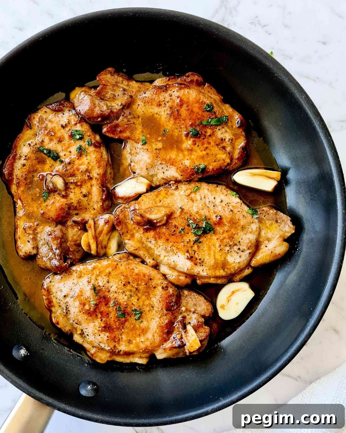 Overhead view of 4 cooked pork chops covered in garlic butter sauce in a black pan