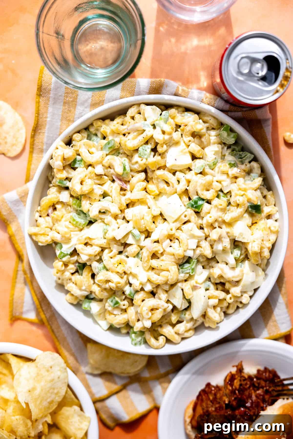 Bowl of macaroni salad on a picnic table with chips and pulled pork nearby.