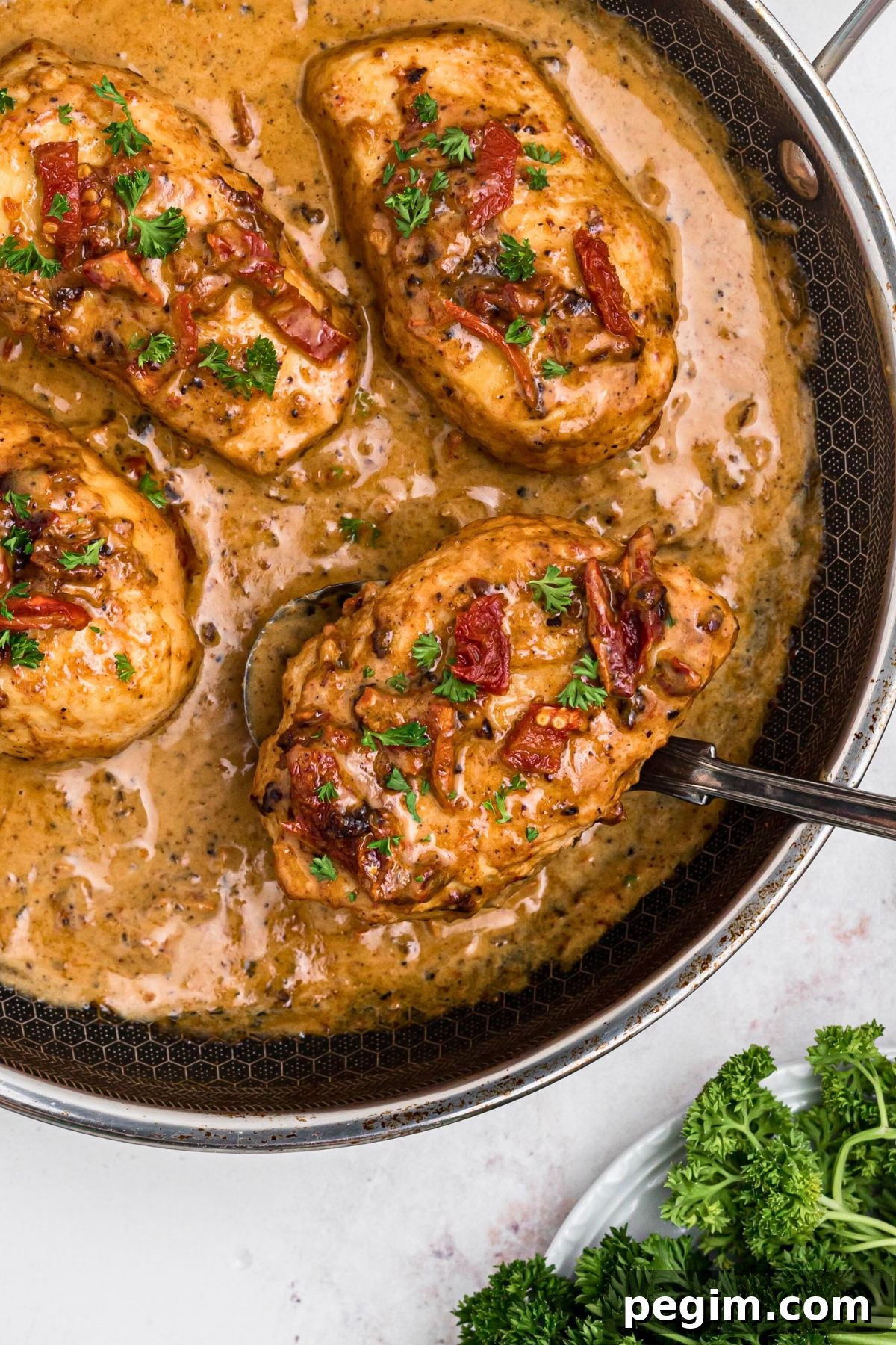 Creamy chicken in a large skillet with a spoon lifting a piece out of skillet. 