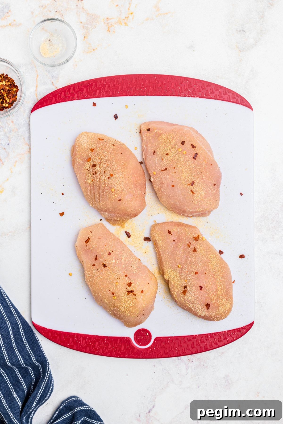 Uncooked chicken being seasoned on a white cutting board. 