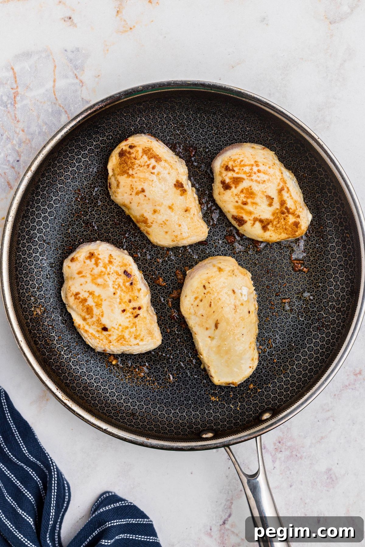 Four chicken breasts seared in a large skillet. 