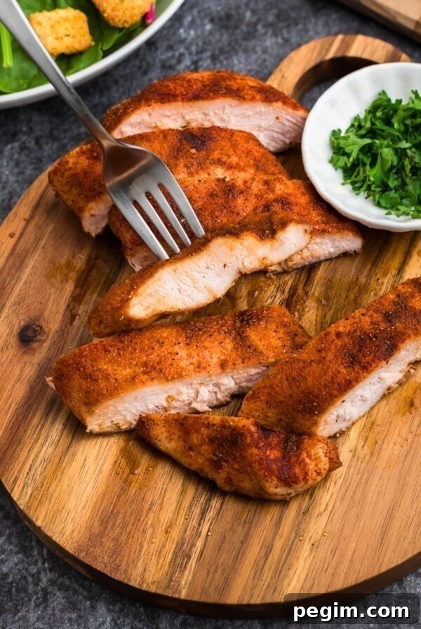 Smoked, seasoned chicken on a small, round cutting board, with parsley flakes in a small cutting board.