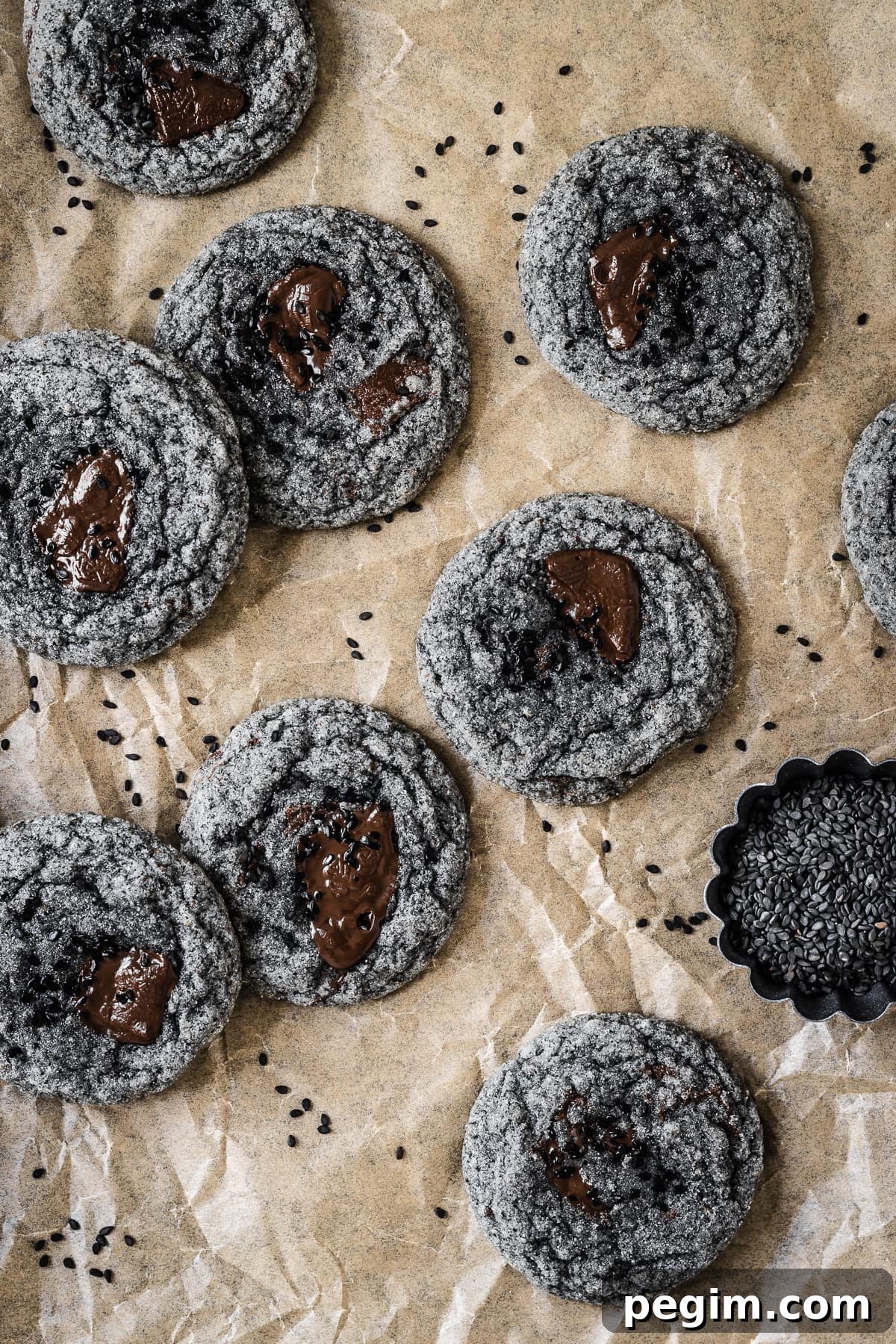 Black sesame cookies with pools of melted chocolate on a brown parchment paper background.