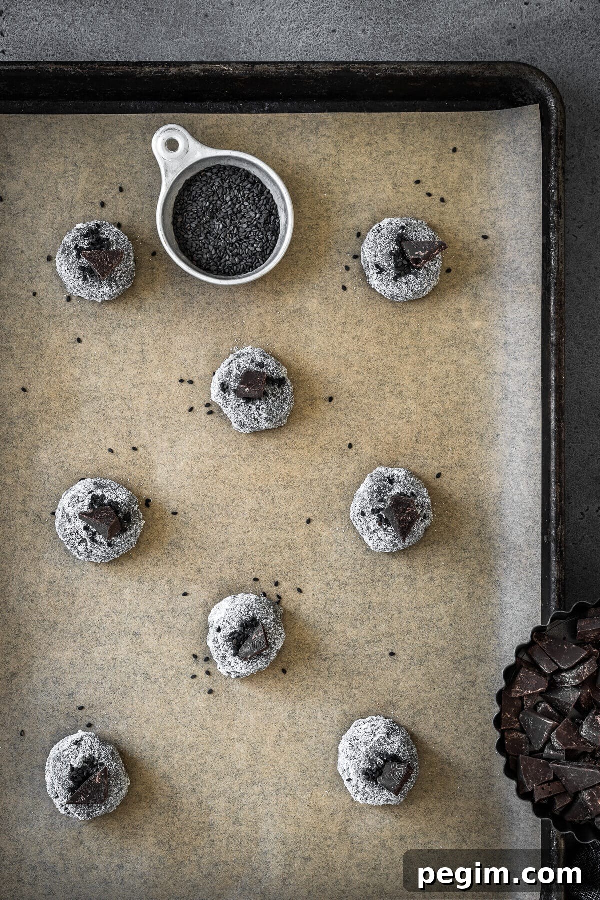 Balls of cookie dough rolled in sugar and topped with black sesame seeds and chocolate chunks.