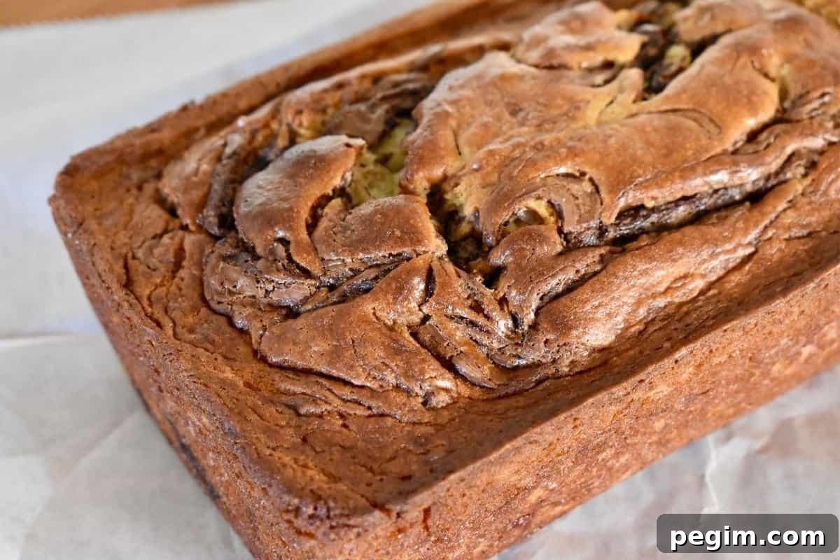 Loaf of Nutella Swirl Banana Bread on a piece of parchment paper on a countertop. 