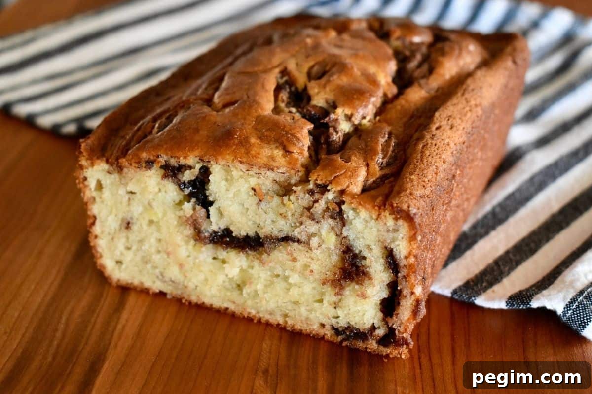 Nutella Swirl Banana Bread on a wood cutting board with a striped towel under it. 
