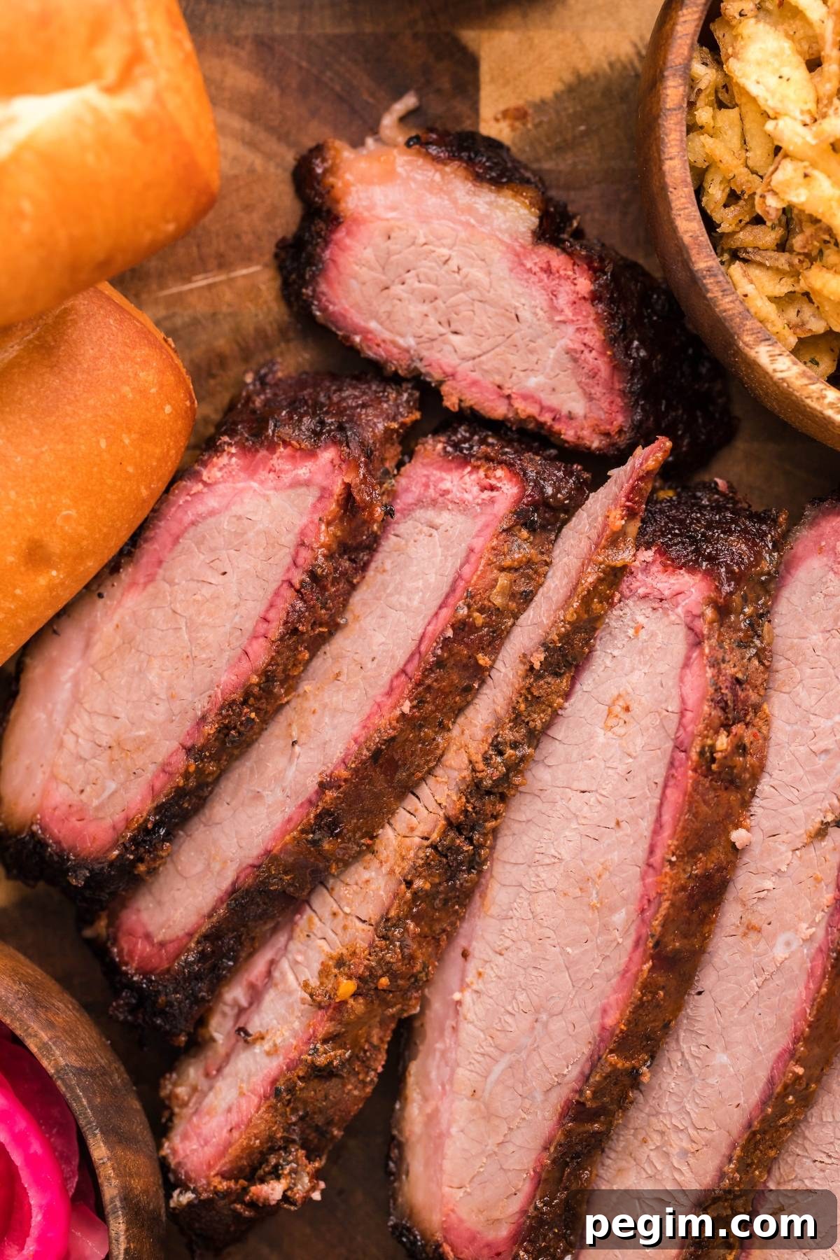 Sliced smoked brisket with a dark bark and pink smoke ring served on bread with pickled onions.