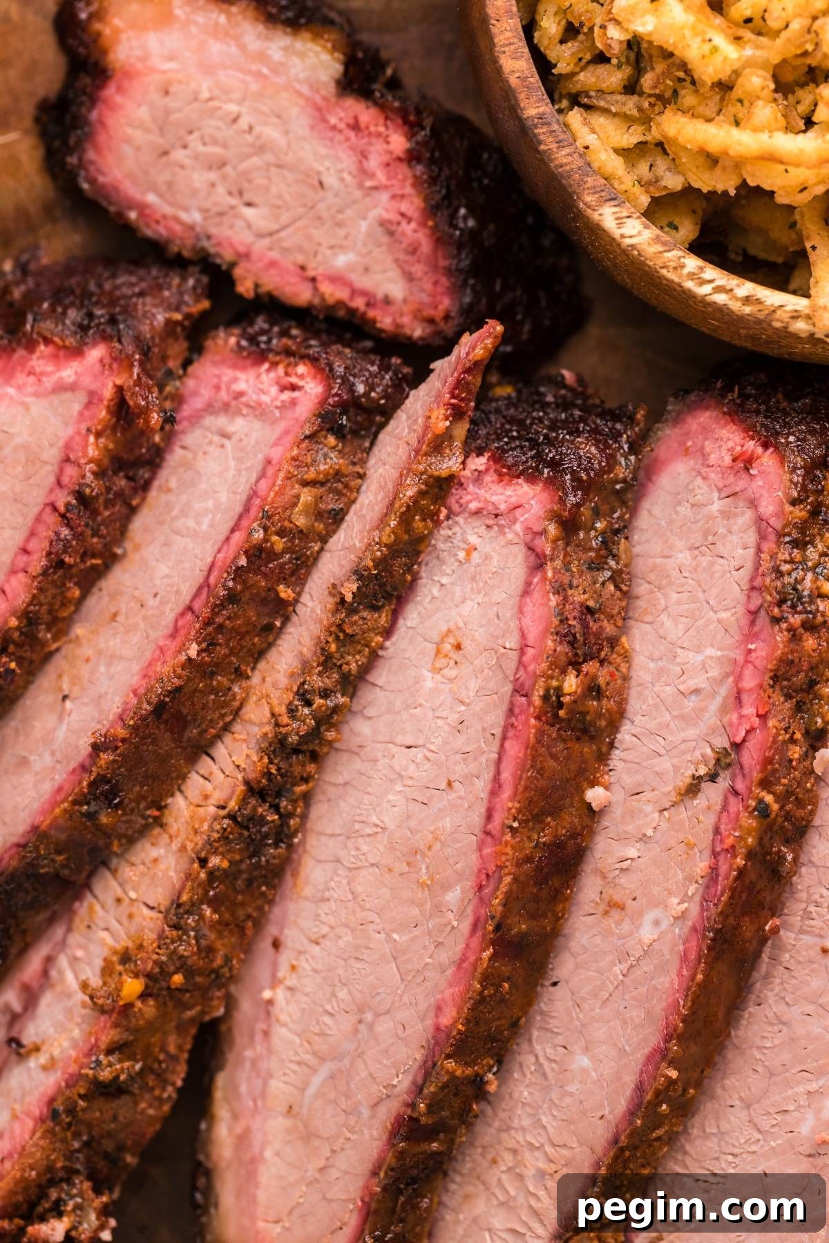 Sliced smoked brisket with a pink smoke ring next to a bowl of crispy fried onions.